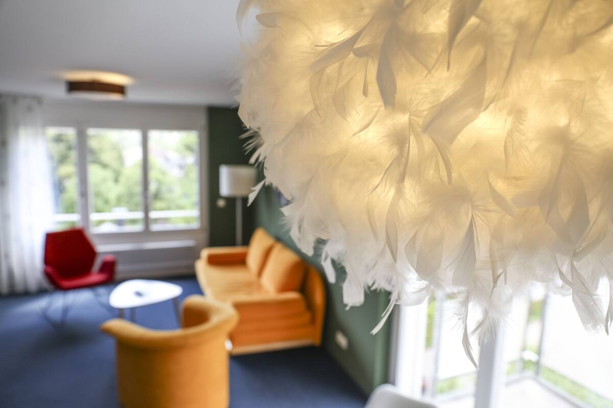 A modern room with a large white feathered installation, a red chair, an orange sofa, and a small white table.