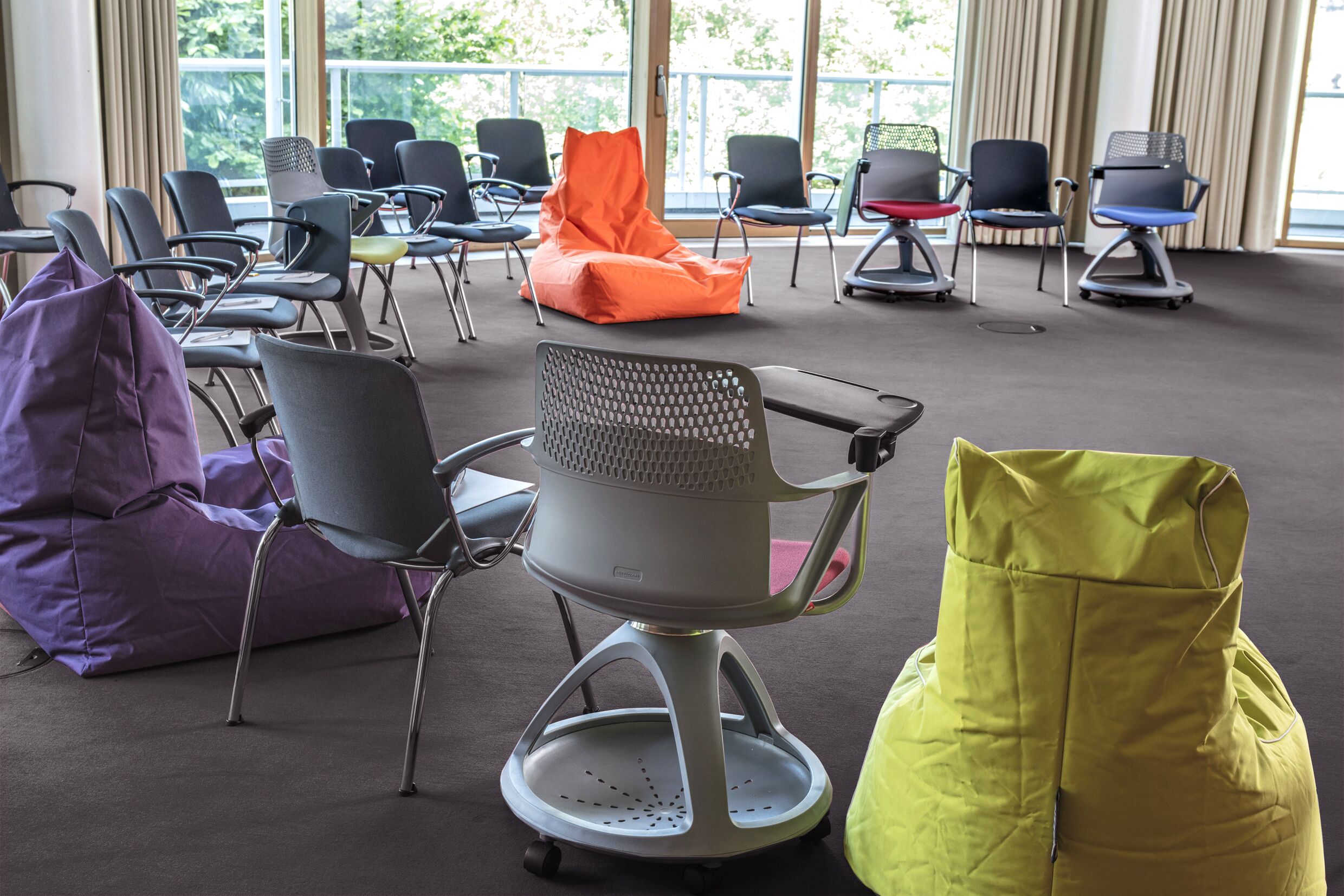 A conference room with multiple chairs and bean bags, large windows with a view of greenery outside.