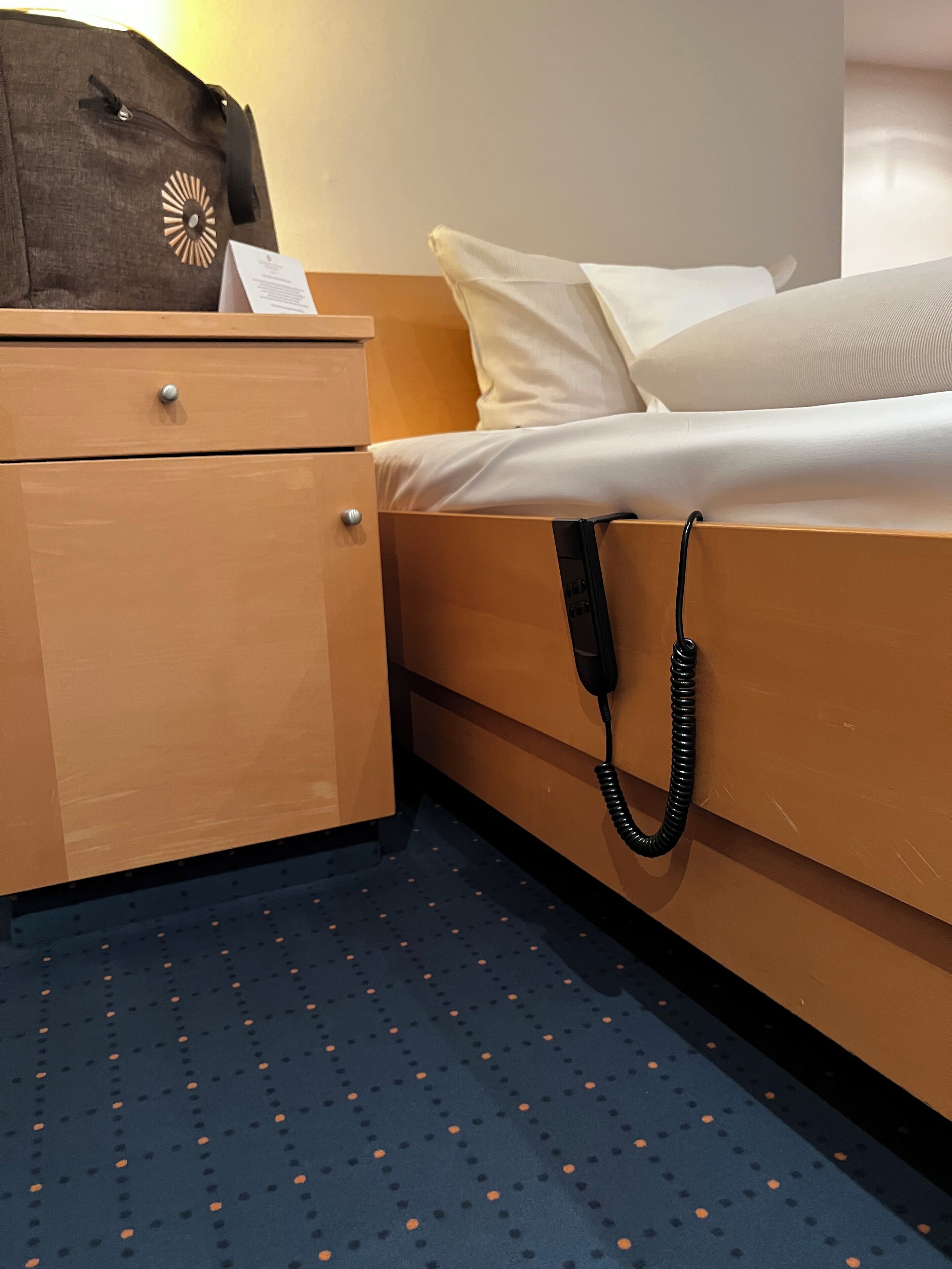Een hotelkamer met een bed, nachtkastje, koffer en telefoon.