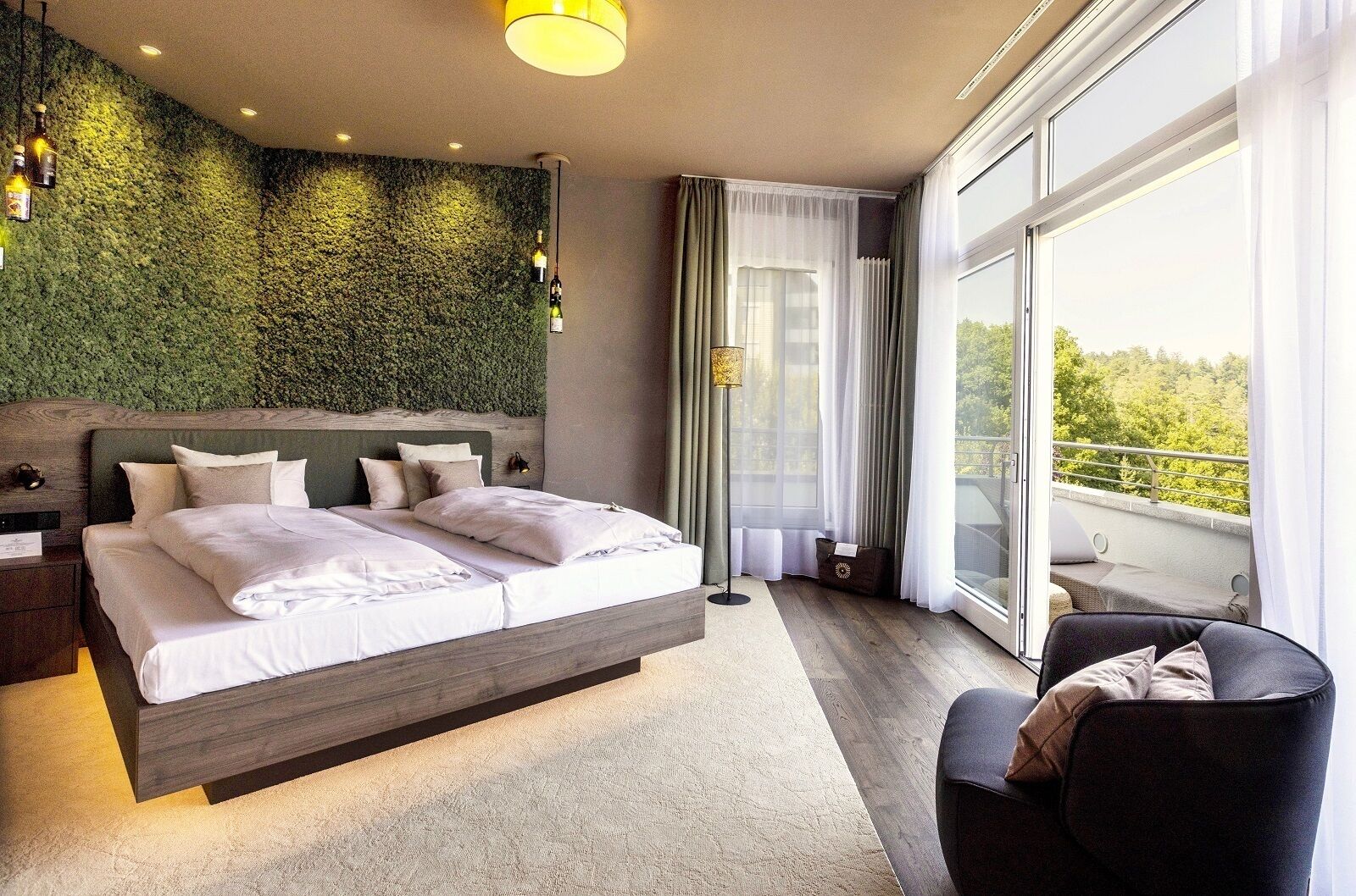 Un dormitorio moderno con una cama grande, una mesita de noche, una silla, un balcón con vistas y una pared verde con textura.