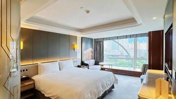 A hotel room with a large bed, a desk, a chair, a TV, and a window with a city view.