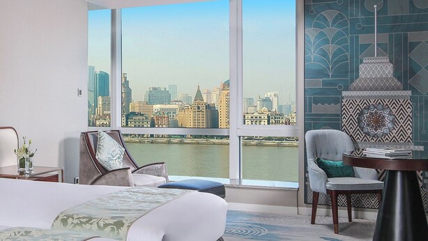 A hotel room with a large window, a bed, two chairs, a small table, and a decorative wall piece. - Oriental Riverside Hotel Shanghai (Shanghai)