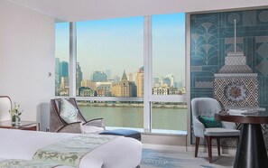 A hotel room with a large window, a bed, two chairs, a small table, and a decorative wall piece. - Oriental Riverside Hotel Shanghai (Shanghai)