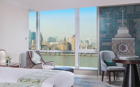 A hotel room with a large window, a bed, two chairs, a small table, and a decorative wall piece.. Oriental Riverside Hotel Shanghai