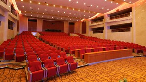 A large auditorium with rows of red chairs, a stage, and a balcony.