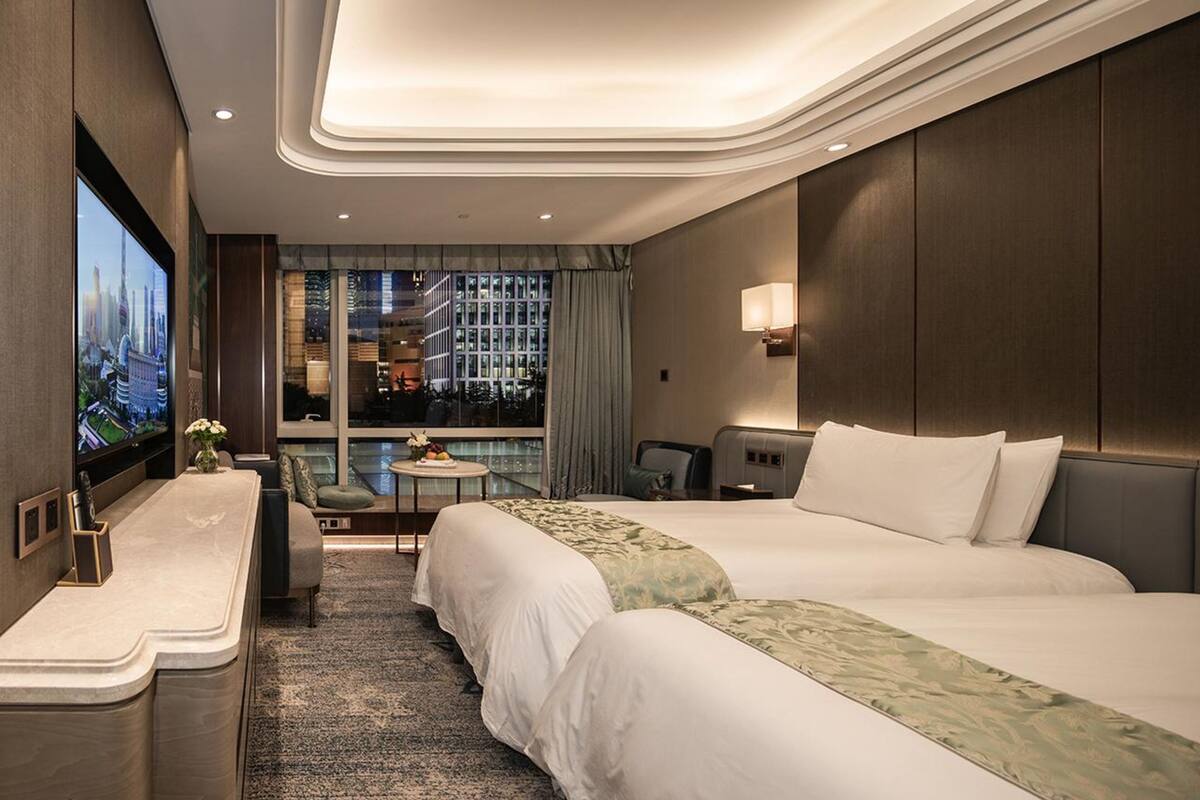 A hotel room with a large bed, a desk, a TV, and a view of a cityscape.