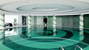 A large indoor swimming pool with a modern design, surrounded by glass walls and a patterned floor.