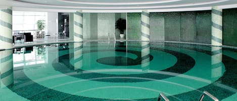 A large indoor swimming pool with a modern design, surrounded by glass walls and a patterned floor.