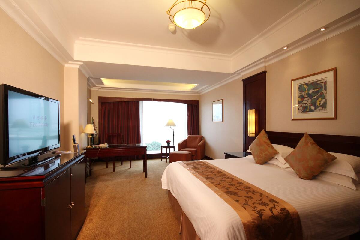 A hotel room with a large bed, a desk with a computer, a television, and a view of the outdoors.