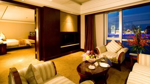 A hotel room with a bed, a TV, a seating area with a table, and a view of a cityscape at night.