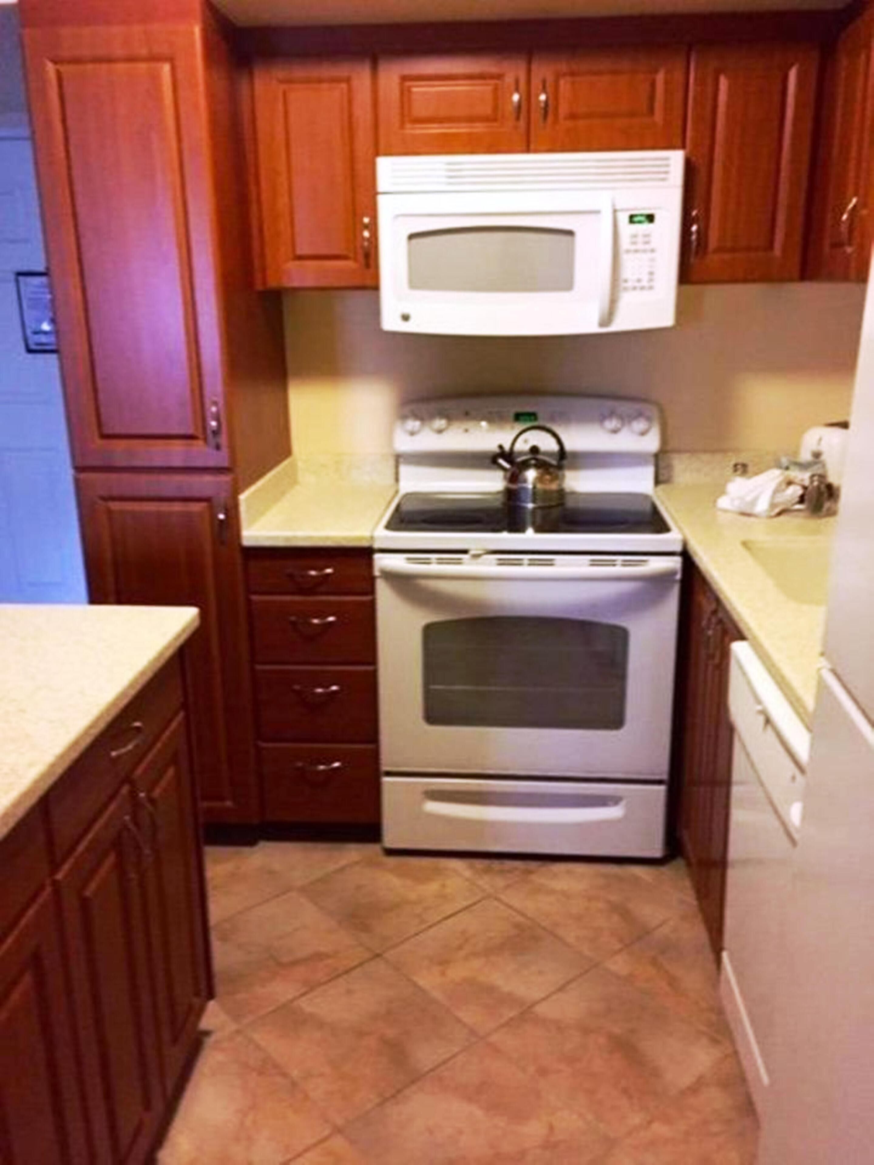 A compact kitchen with wooden cabinets, a built-in microwave, a stove, and a refrigerator.
