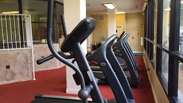 A row of treadmills in a gym with a red carpet floor, large windows, and a white door in the background.