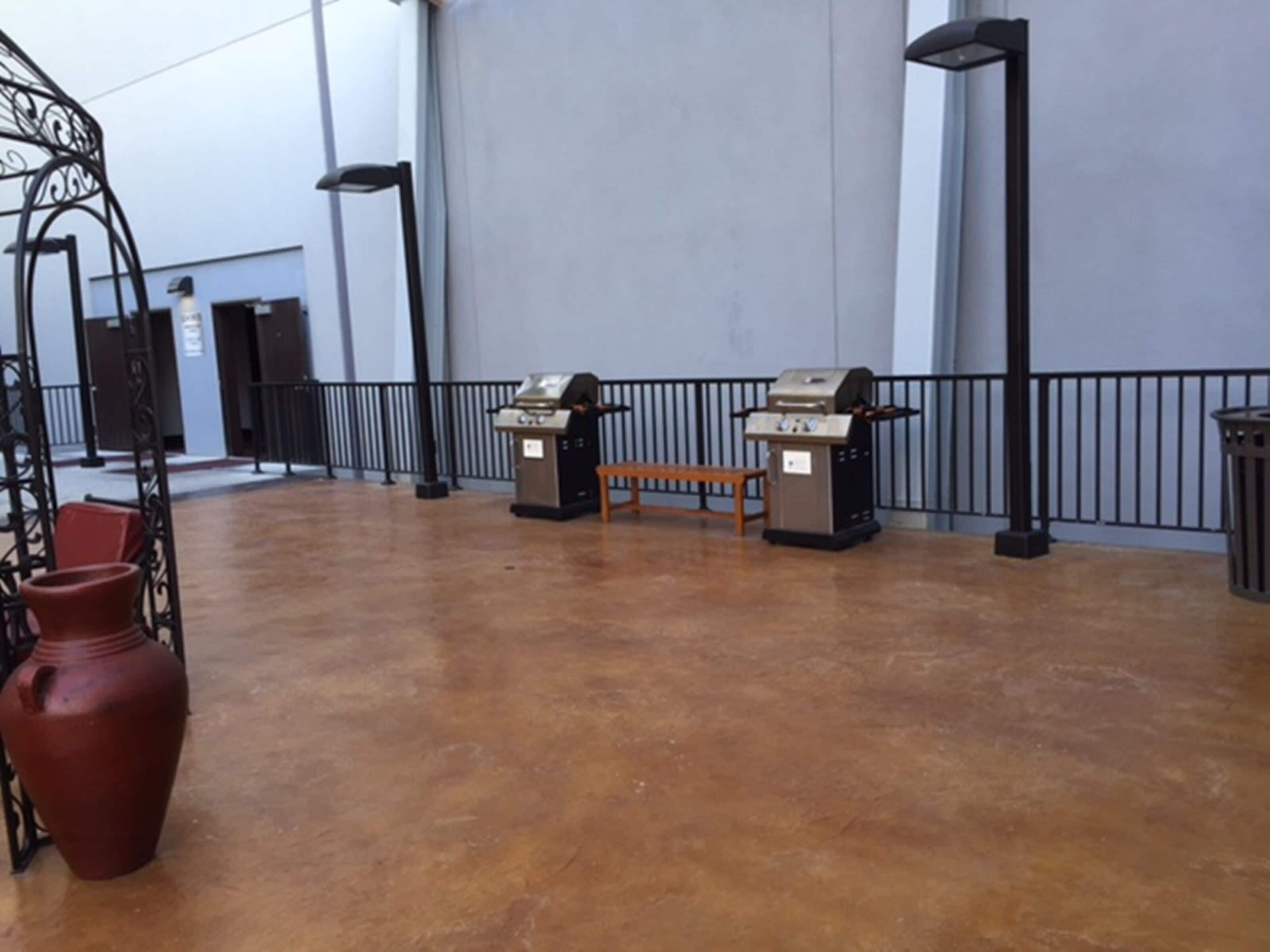 An indoor area with a concrete floor, two barbecue grills, a wooden bench, and a red vase.