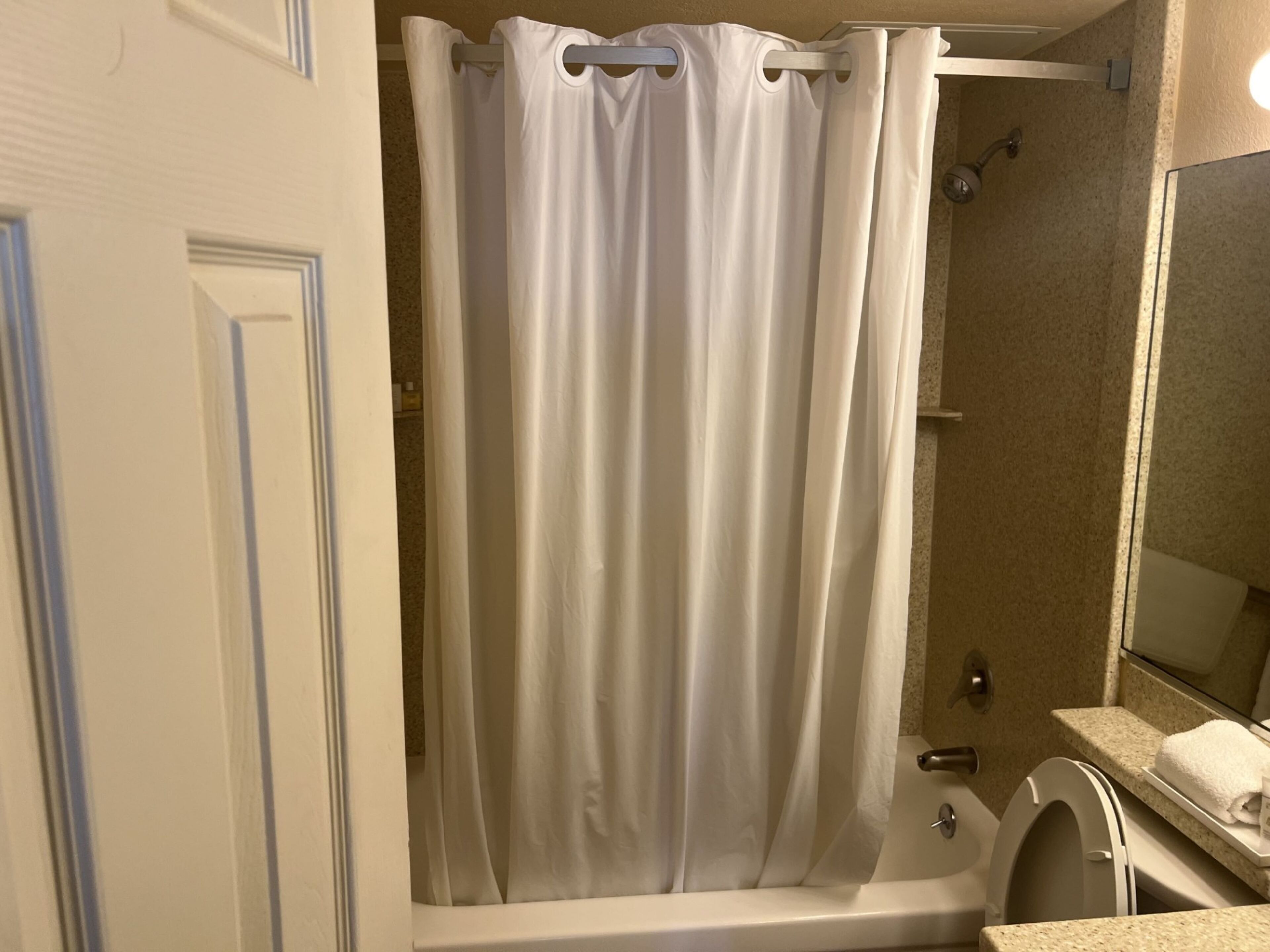 Een badkamer met douchegordijn, bad, toilet en wastafel.
