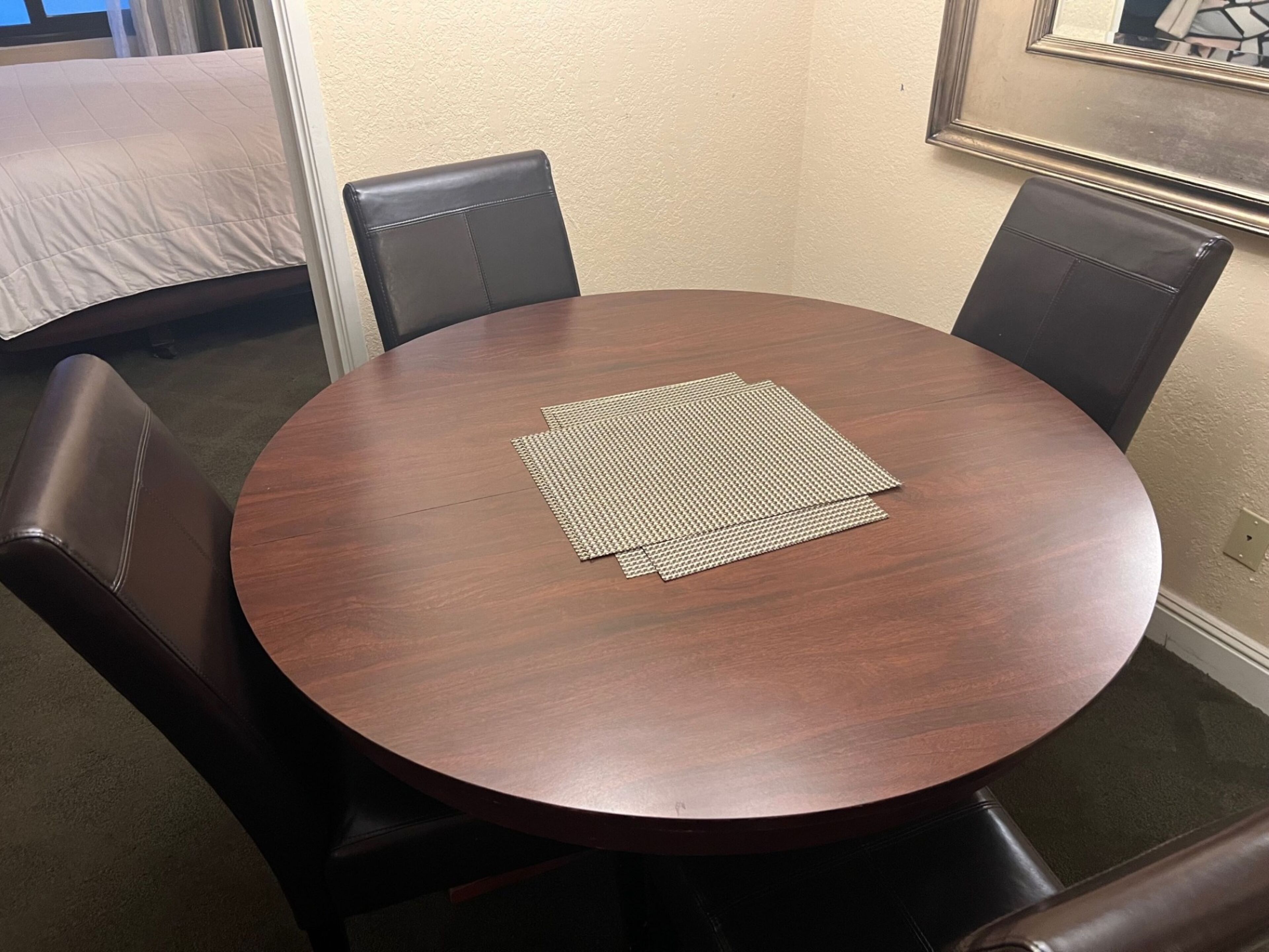 A round wooden table with a woven placemat, surrounded by four black leather chairs.