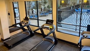 Un gimnasio con cintas de correr, un teléfono y vistas a un patio exterior.