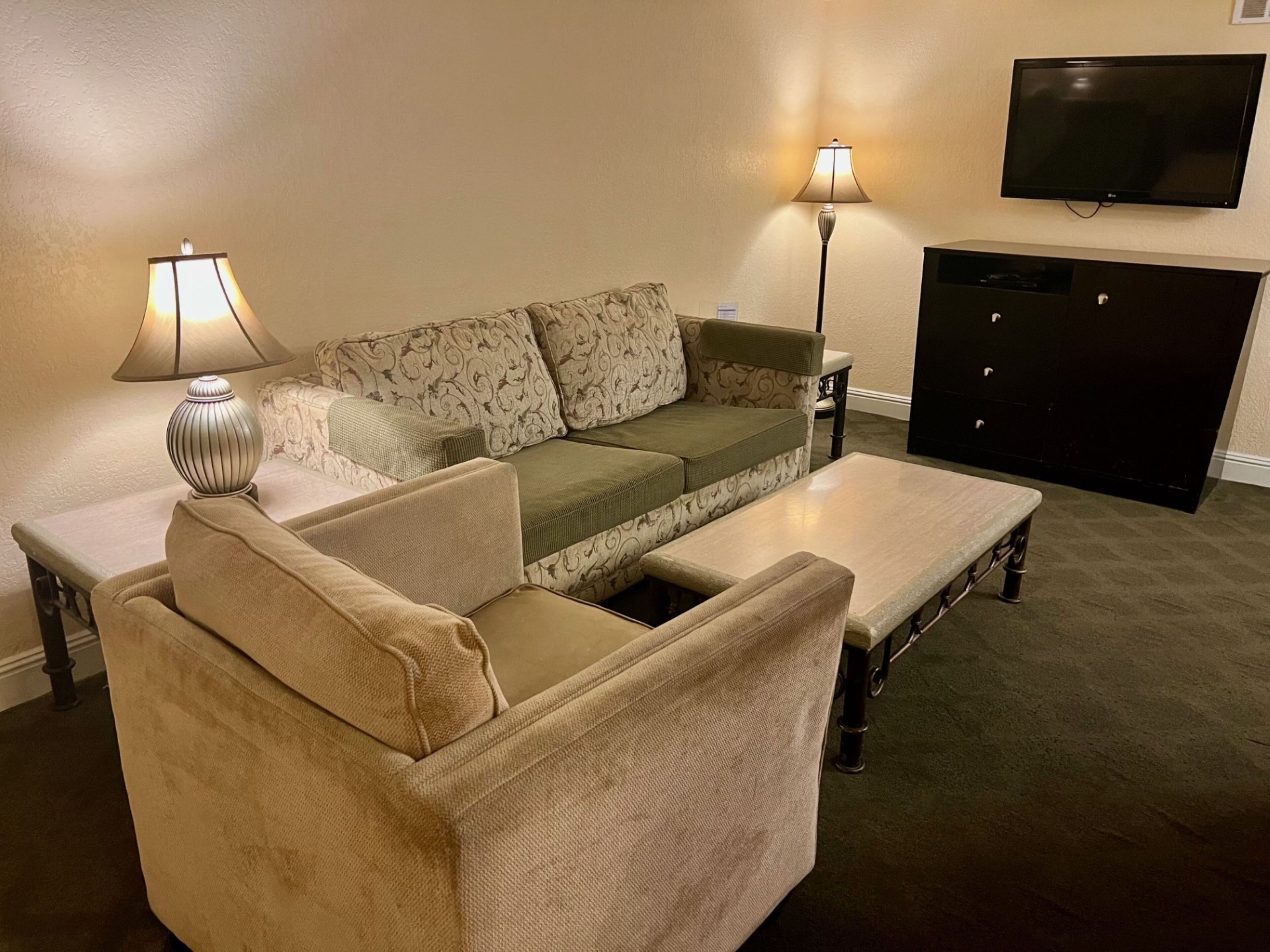 A living room with a sofa, armchair, coffee table, two lamps, and a TV.