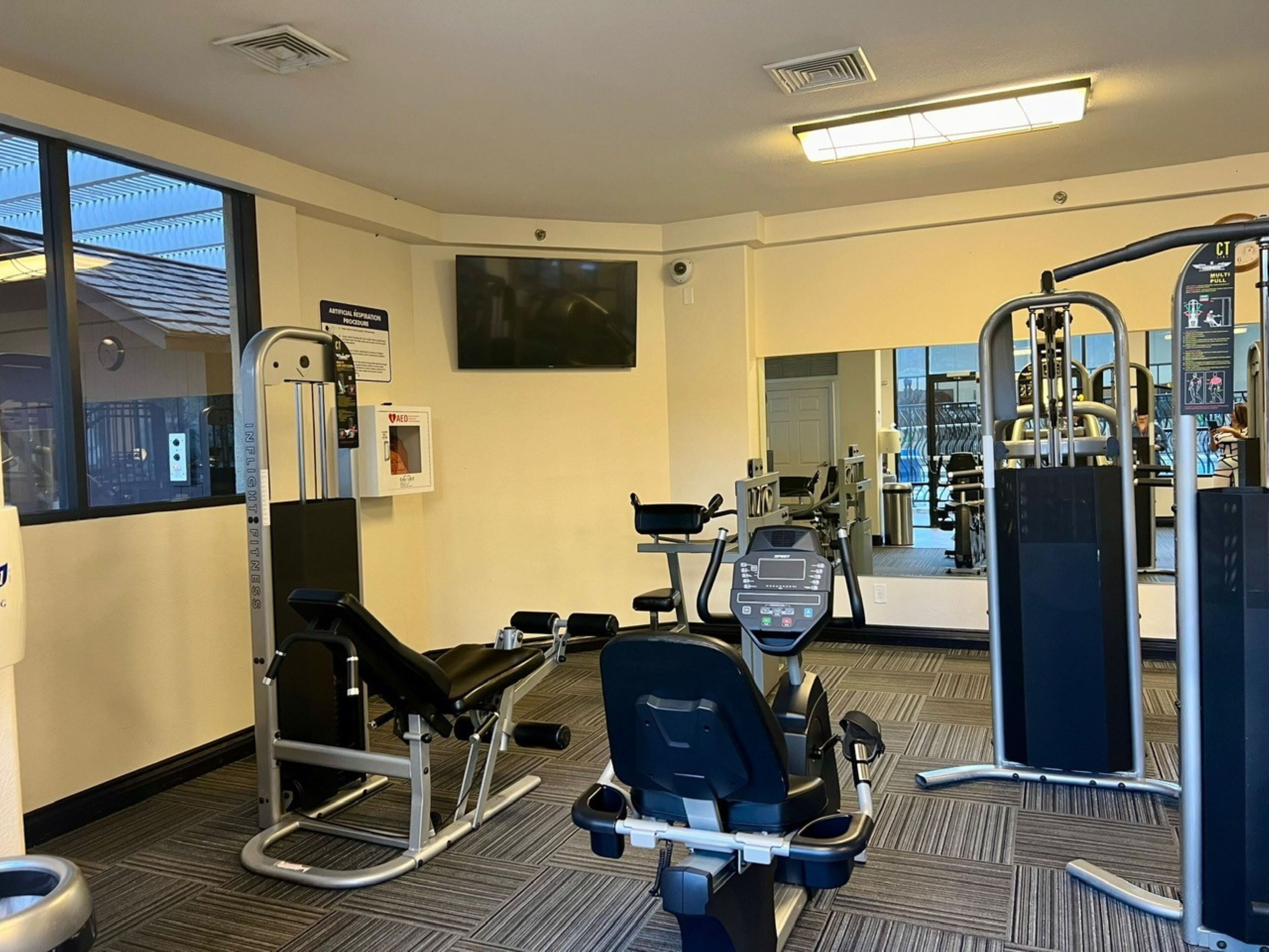 Et fitnesscenter med træningsudstyr, et stort spejl og udsigt ud af et vindue.