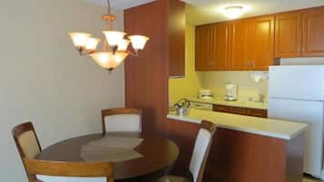 A compact kitchen with wooden cabinets, a white refrigerator, a coffee maker, and a chandelier.