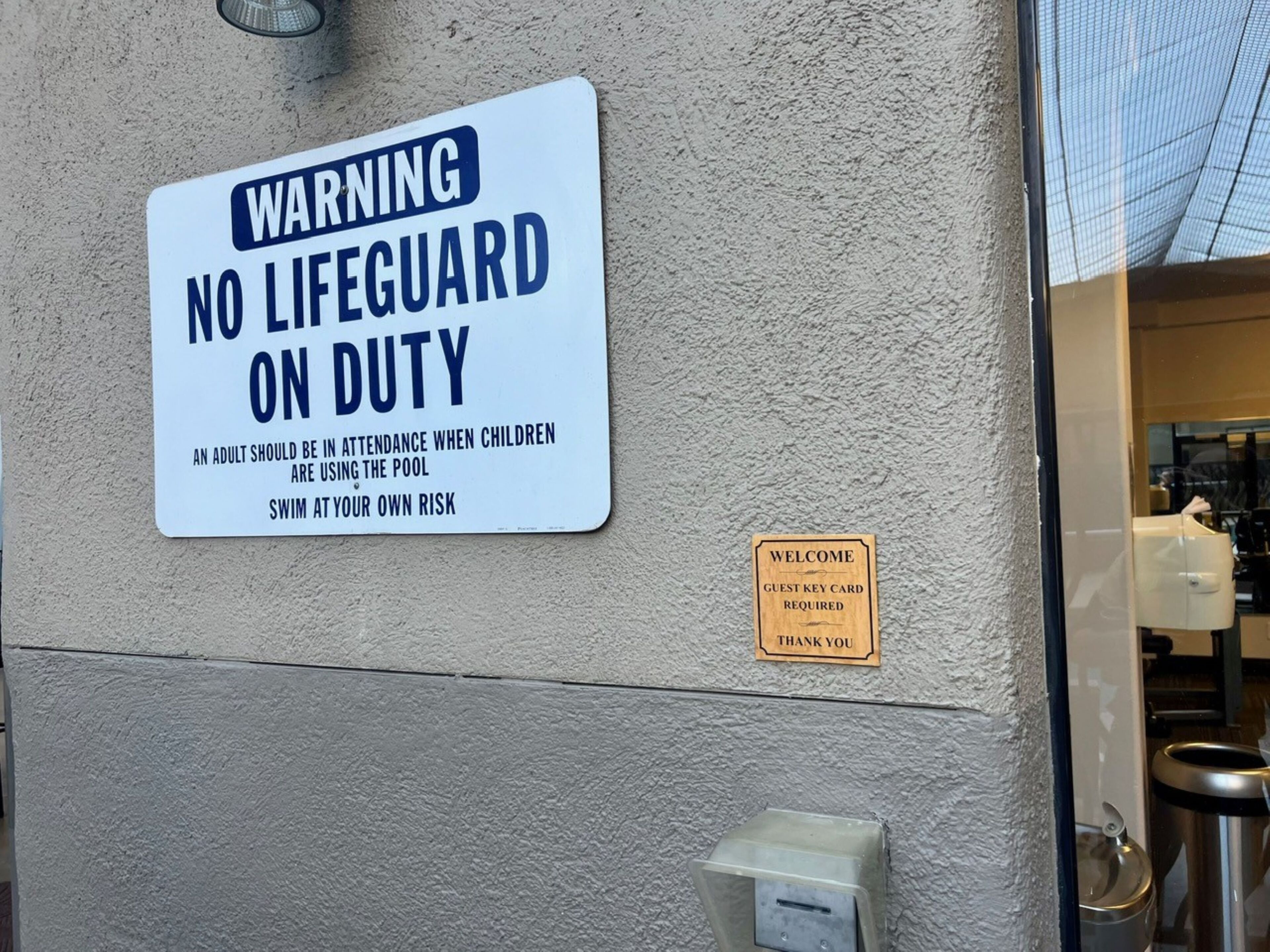 A warning sign stating 'No Lifeguard on Duty' and a 'Welcome' sign with a guest key card requirement.