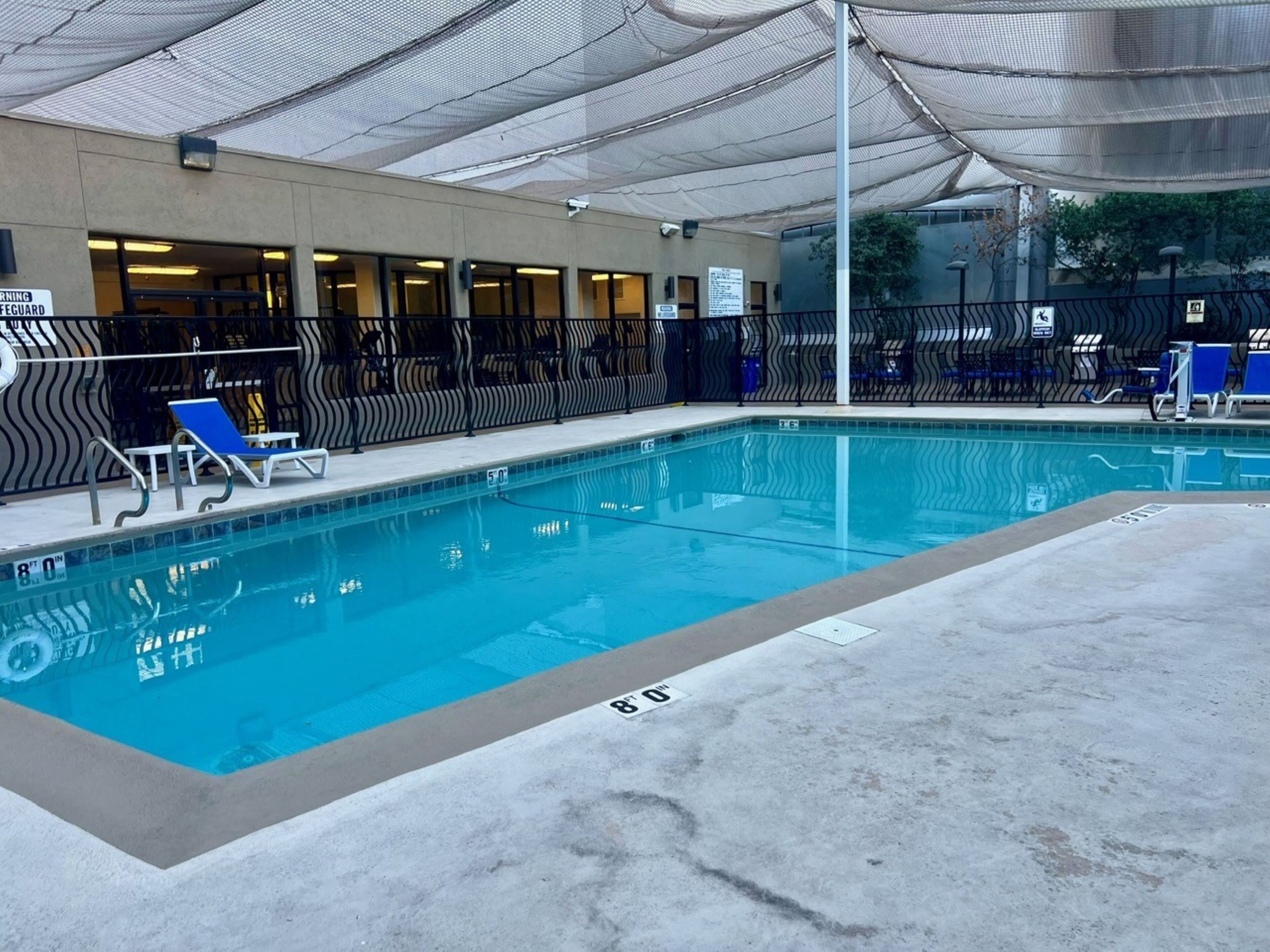 A swimming pool with blue water, surrounded by lounge chairs and a covered area with a patterned fence.