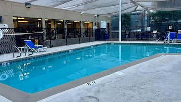 A swimming pool with blue water, surrounded by lounge chairs and a covered area with a patterned fence.
