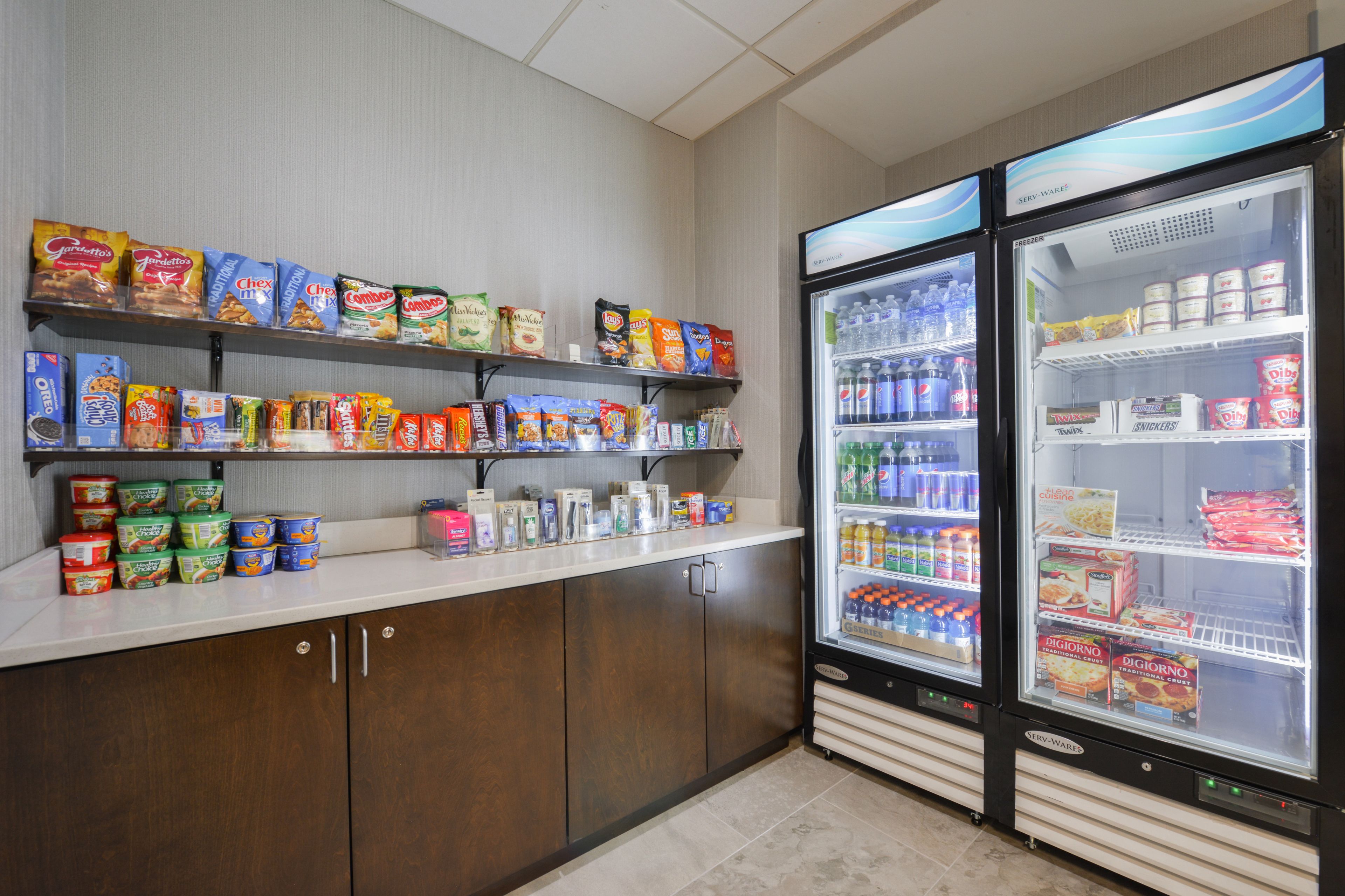 A self-service snack and beverage area with refrigerated drink dispensers and shelves stocked with various snacks and beverages.