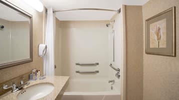 A bathroom with a sink, mirror, shower, and framed artwork on the wall.