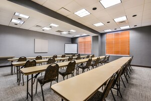 Uma sala de conferências com várias mesas e cadeiras, uma lousa e um projetor.