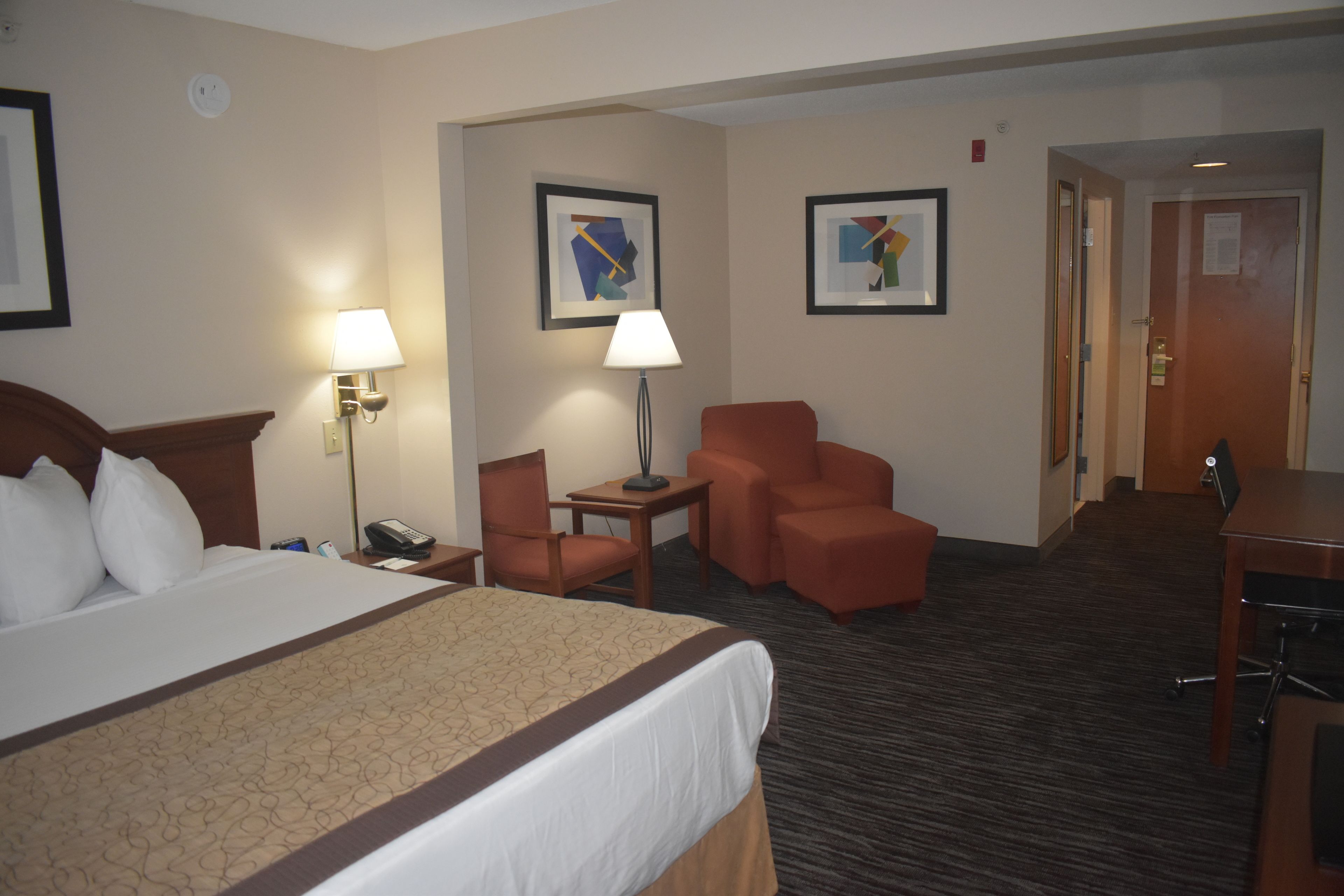 A hotel room with a large bed, two chairs, a desk, and a lamp.