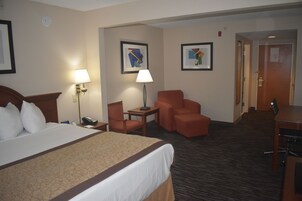 A hotel room with a large bed, two chairs, a desk, and a lamp.