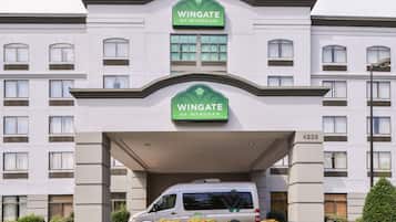 A Wingate by Wyndham hotel with a white facade, multiple windows, and a van parked in front.