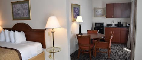 Ett hotellrum med en säng, en sänglampa, ett litet bord med stolar, en mikrovågsugn och ett litet pentry.