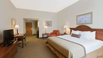 A hotel room with a large bed, a desk with a television, two lamps, and framed artwork on the walls.