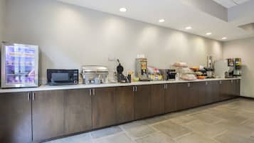 Een moderne keuken met een koelkast, magnetron, koffiezetapparaat en diverse etenswaren op het aanrecht.