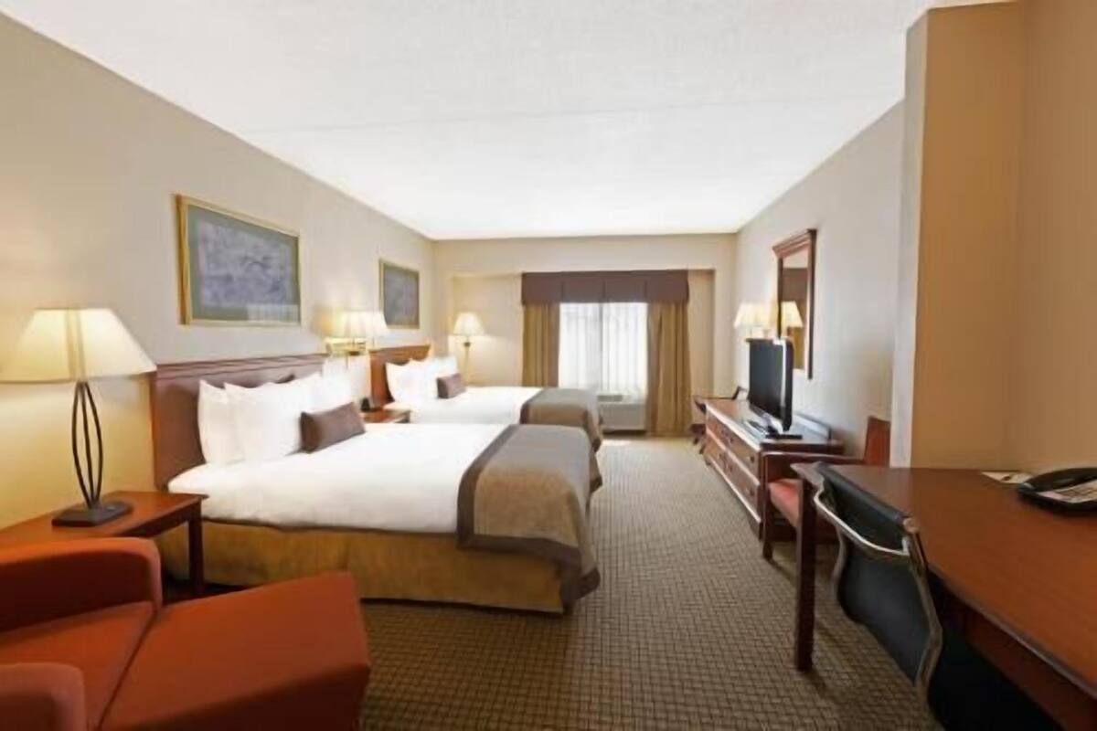 A hotel room with two beds, a desk, a chair, a TV, and a window with curtains.