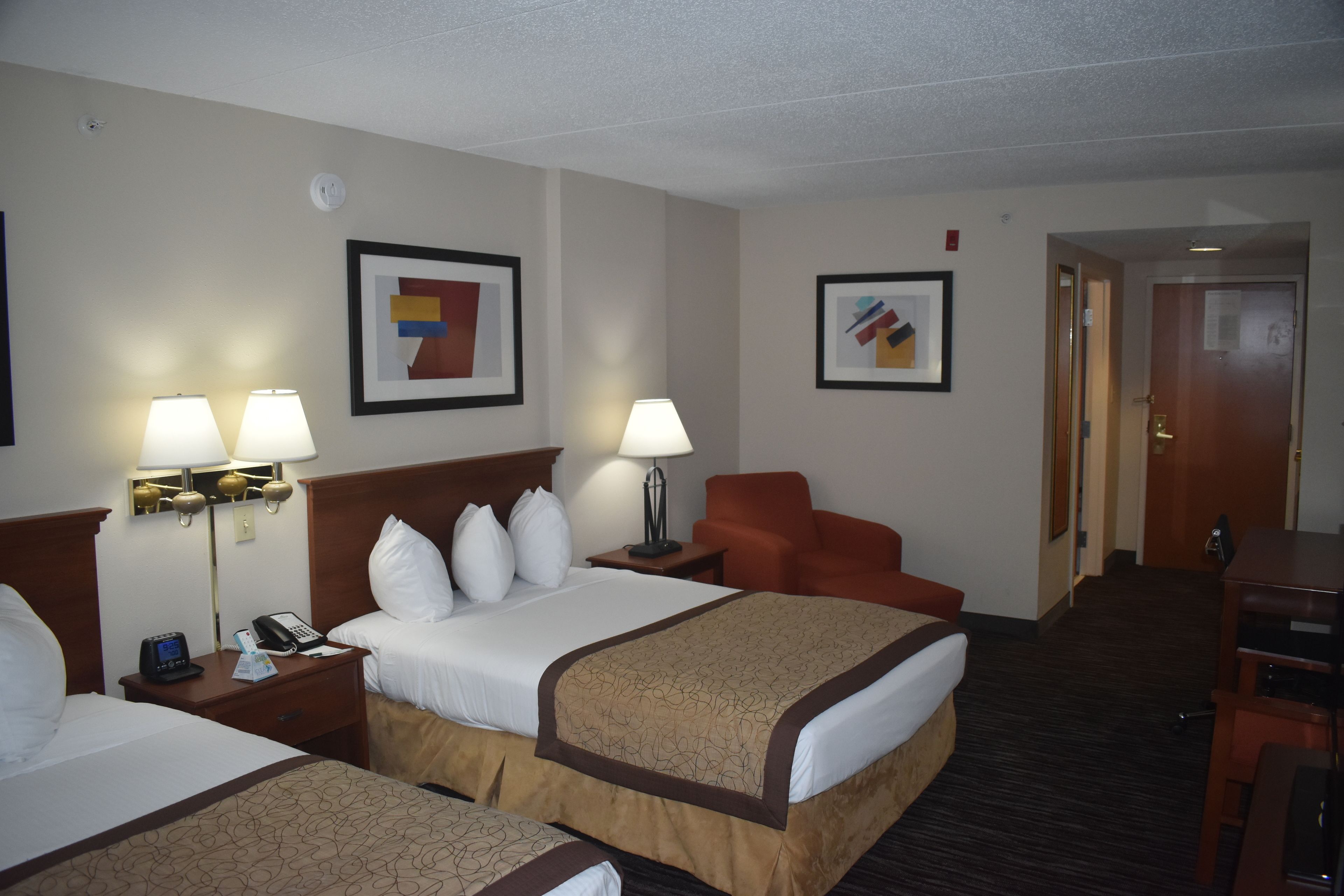 A hotel room with two beds, a desk, a chair, and artwork on the walls.