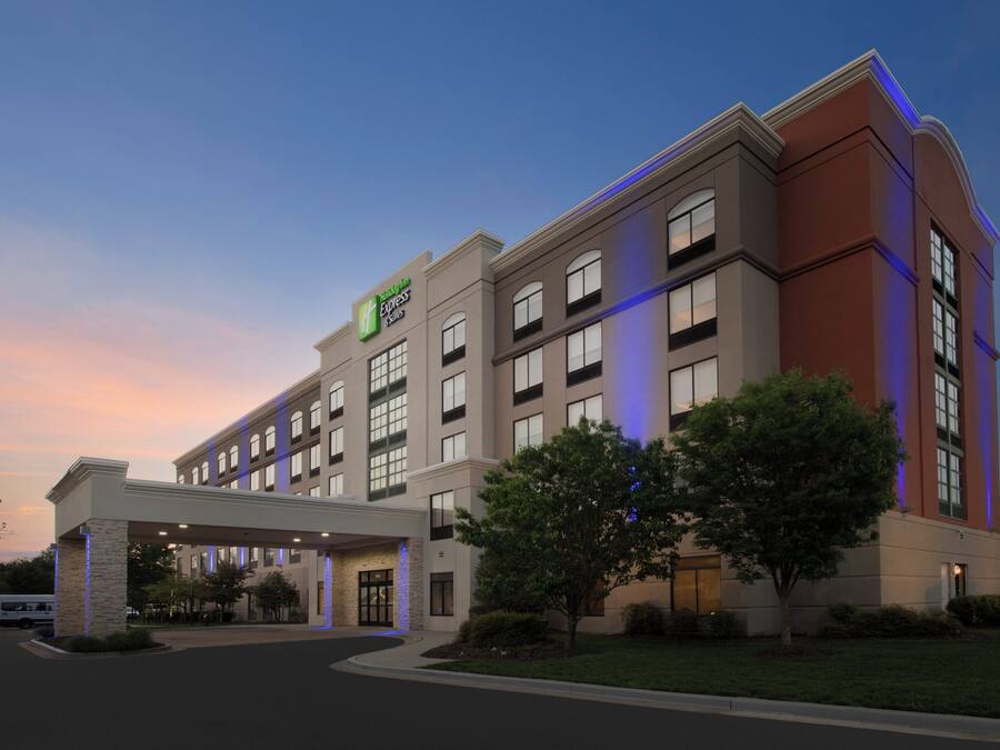 A multi-story hotel with a prominent Holiday Inn Express & Suites sign, a covered entrance, and a landscaped front yard.