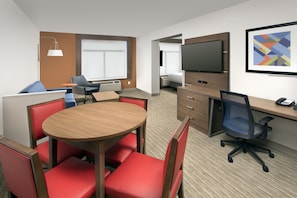A hotel room with a round wooden table, red chairs, a TV, a desk with a computer, and a bed in the background. - Holiday Inn Express & Suites Baltimore - BWI Airport North by IHG (Linthicum Heights)