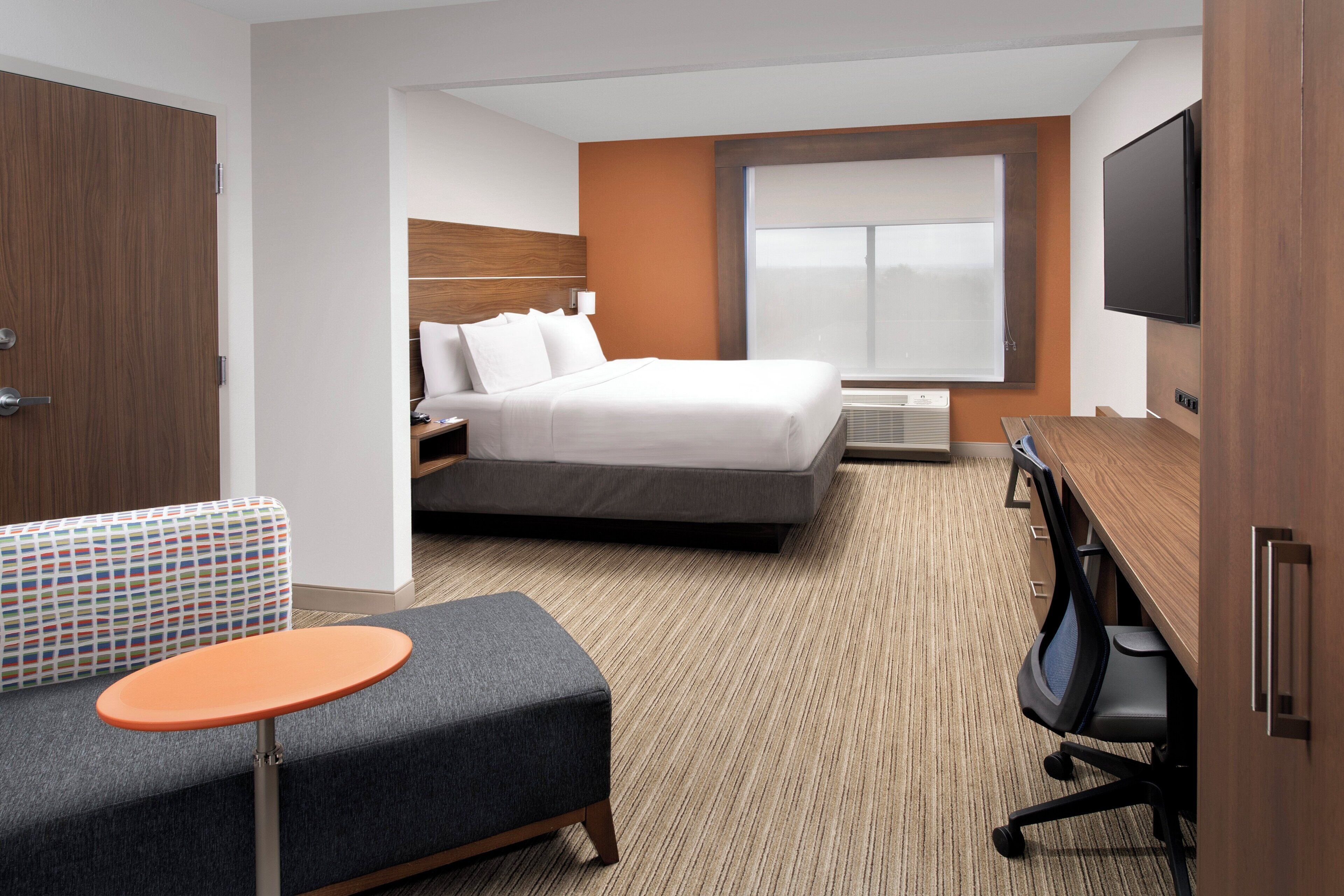 Habitación de hotel con cama, escritorio, silla, una mesita y televisor.