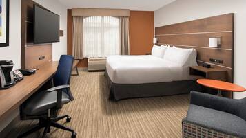 A hotel room with a bed, desk, chair, TV, and a small table.