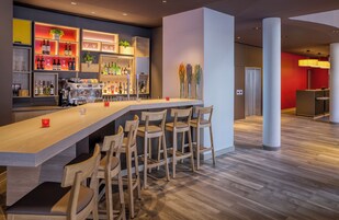 Uma área de bar com um balcão comprido, vários bancos e prateleiras repletas de garrafas e copos.