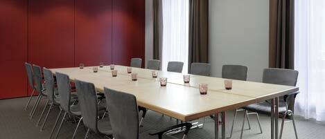 A conference room with a long table, grey chairs, and a red accent wall.