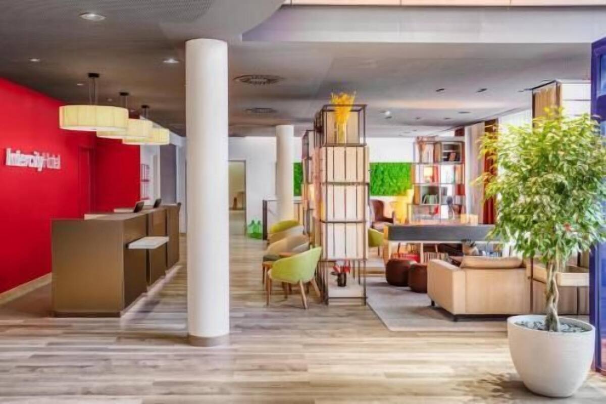A modern hotel lobby with a reception desk, seating area, and a large potted plant.