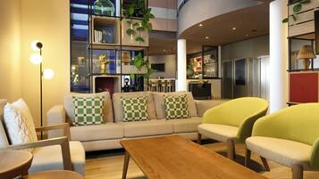 A modern interior with a sofa, chairs, a wooden table, and a kitchen area with plants.