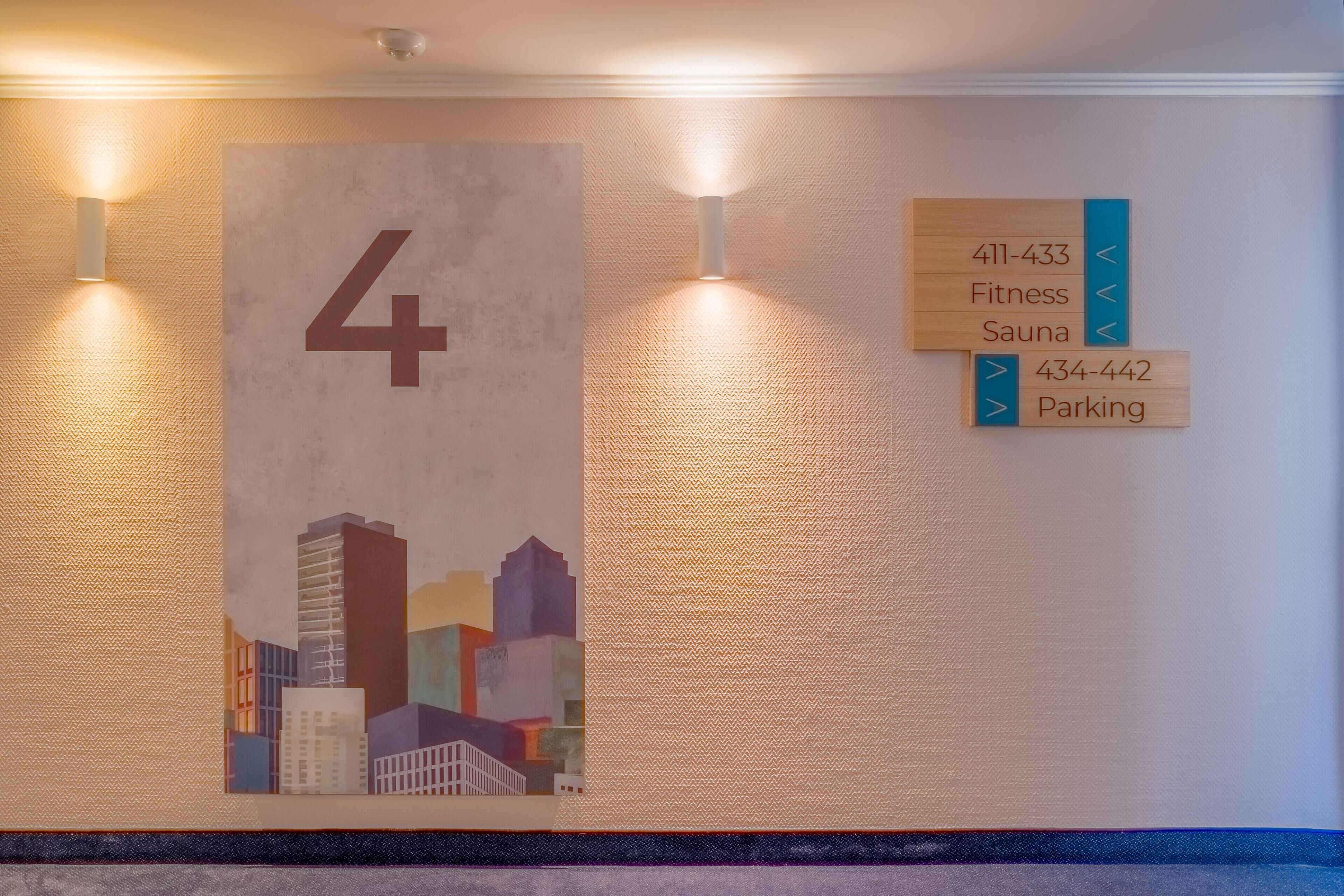 Pared con el número '4' en grande y flechas direccionales que indican acceso a servicios como gimnasio, sauna y estacionamiento, junto con sus números de teléfono.
