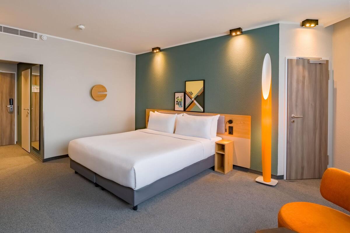 Ein Hotelzimmer mit Bett, Nachttisch, Lampe und einer Tür.