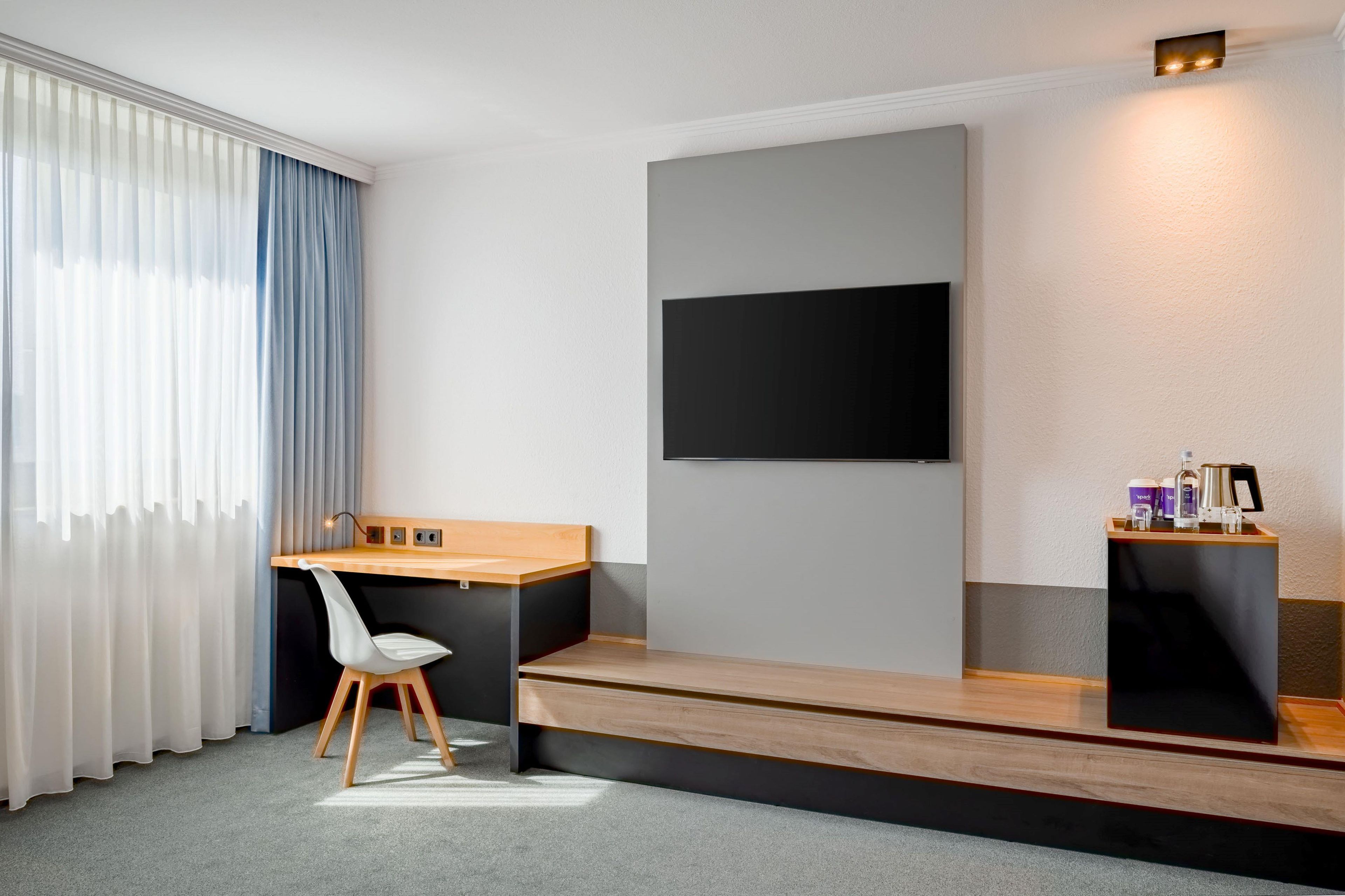 Een moderne hotelkamer met een bureau, stoel en een wandgemonteerde flatscreen televisie.