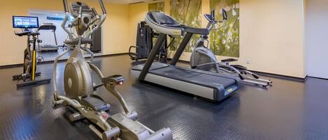 A gym with various cardio machines, a digital screen, and a patterned floor.