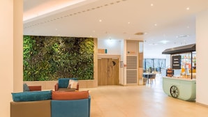 A lobby with a green wall, a seating area with a sofa and chairs, a reception desk, and a bar area.
